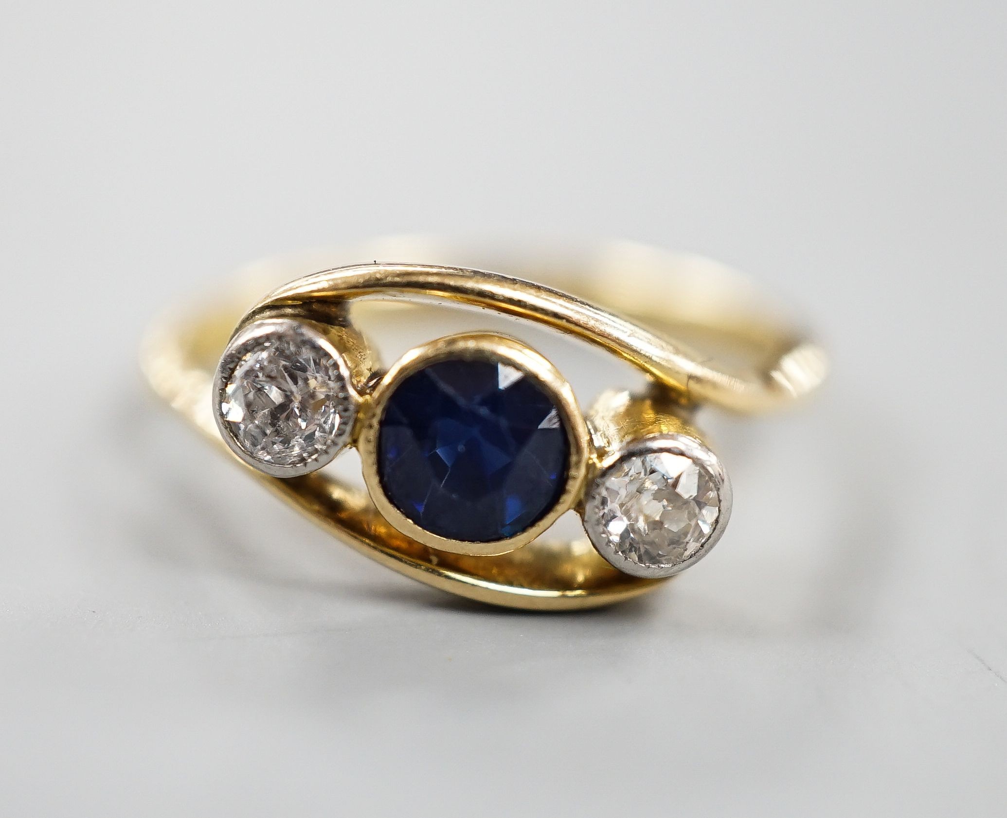 A modern 18ct gold, single stone diamond and two sapphire set crossover ring, size K, gross 3.2 grams.